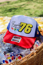 Baseball cap with number 76 and colorful design in a basket with disco ball and snacks, flat lay frontal view