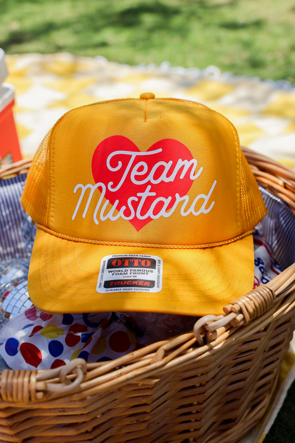 Yellow trucker at with 'Team Mustard' text and red heart in a wicker basket outdoors, frontal view