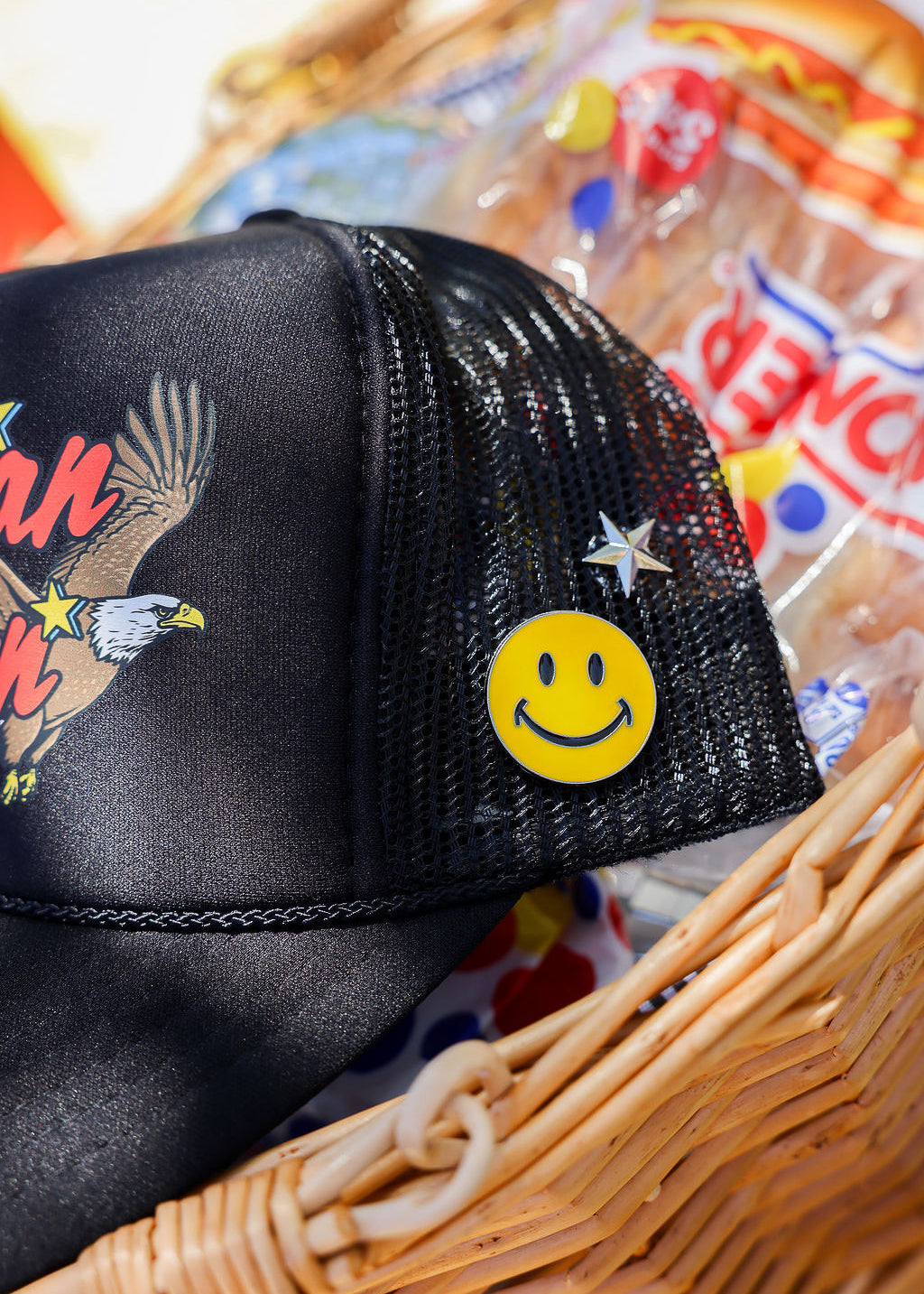 Black mesh trucker hat with smiley face pin in a basket
