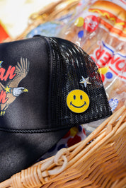 Black mesh trucker hat with smiley face pin in a basket