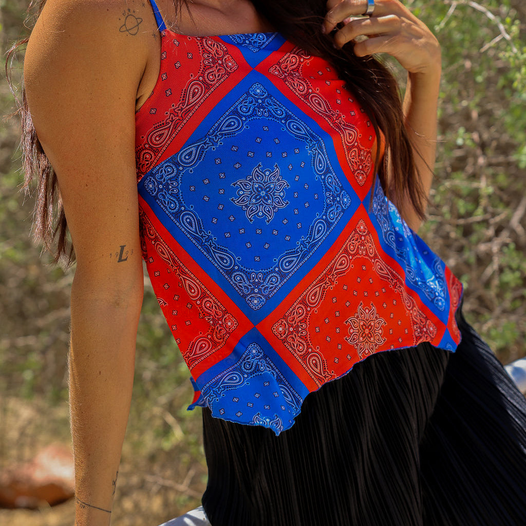 Model wearing a red and blue bandana patterned tank mesh top with black shorts outdoors, close up frontal view