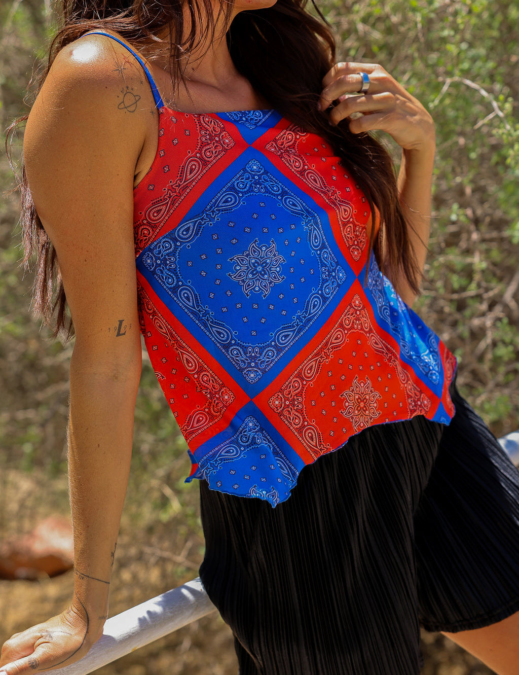 Model wearing a red and blue bandana patterned tank mesh top with black shorts outdoors, close up frontal view