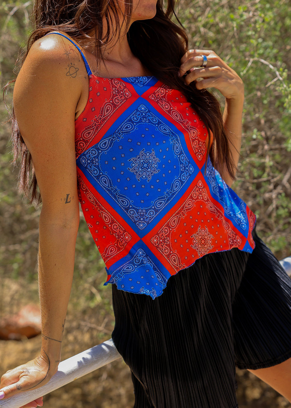 Model wearing a red and blue bandana patterned tank mesh top with black shorts outdoors, close up frontal view