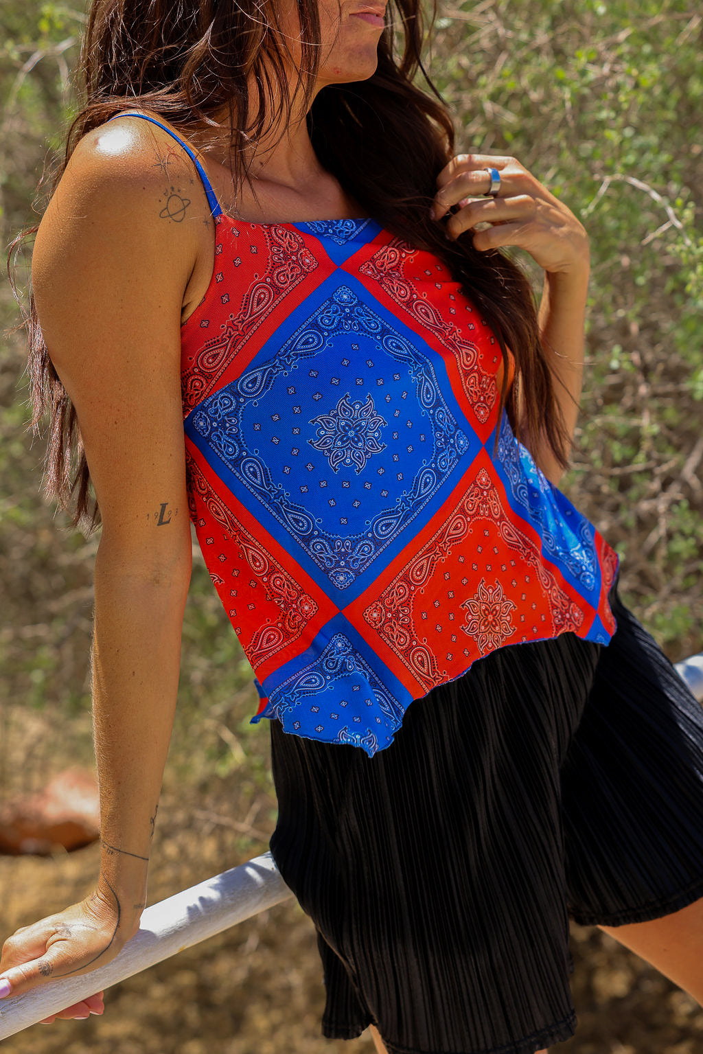 Model wearing a red and blue bandana patterned tank mesh top with black shorts outdoors, close up frontal view