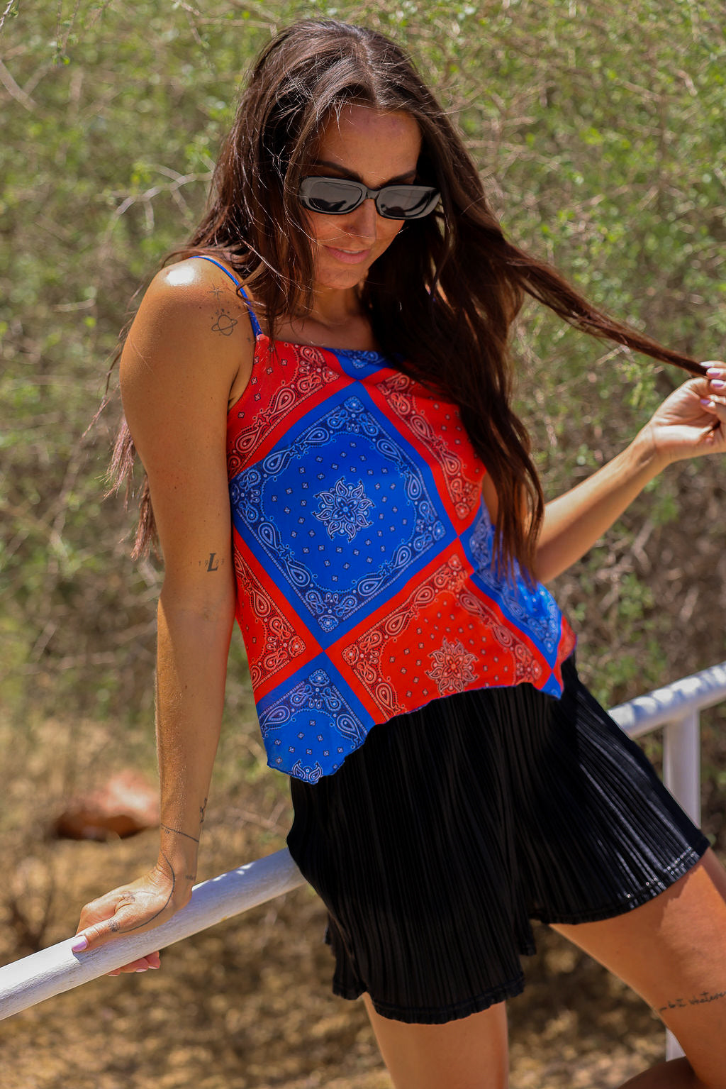 Model wearing a red and blue bandana patterned tank mesh top with black shorts outdoors, close up side view