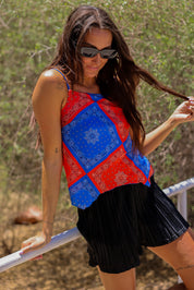 Model wearing a red and blue bandana patterned tank mesh top with black shorts outdoors, close up side view