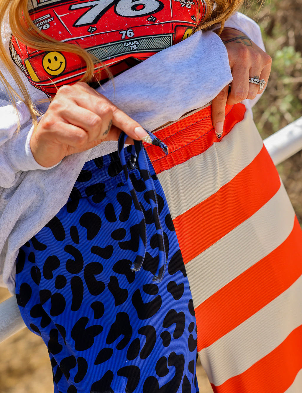 Model wearing a grey crewneck with number 76, blue pants with black spots, and red and ivory stripes, close up of waistband