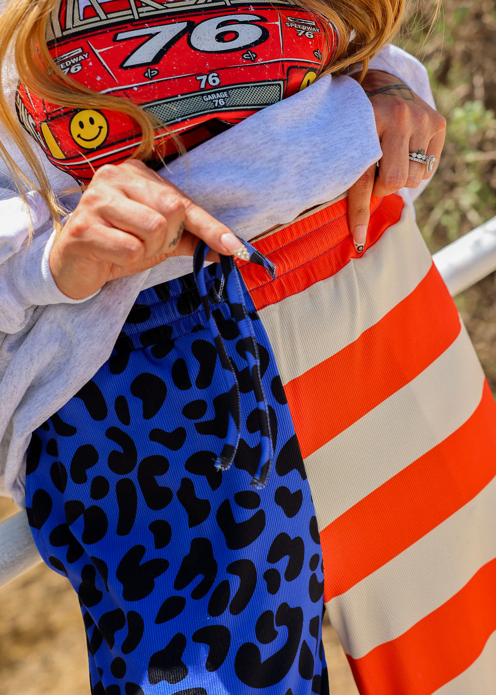 Model wearing a grey crewneck with number 76, blue pants with black spots, and red and ivory stripes, close up of waistband