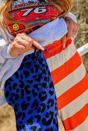 Model wearing a grey crewneck with number 76, blue pants with black spots, and red and ivory stripes, close up of waistband