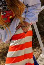 Person wearing a red and white striped pants and grey crewneck with hand in pocket, with a blurred background, close up side view