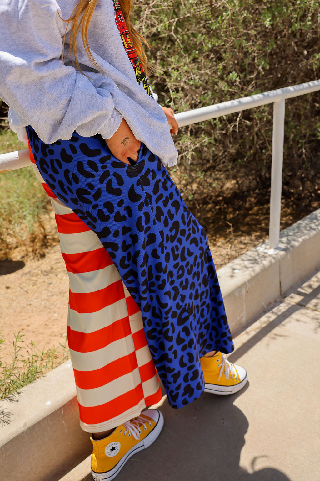Model wearing blue leopard print pants with red and white striped pattern, standing outdoors, side view