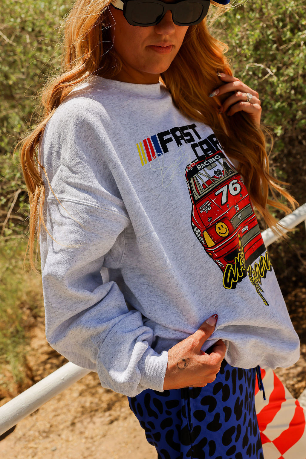 Person wearing a gray sweatshirt with a race car graphic design outdoors, side view