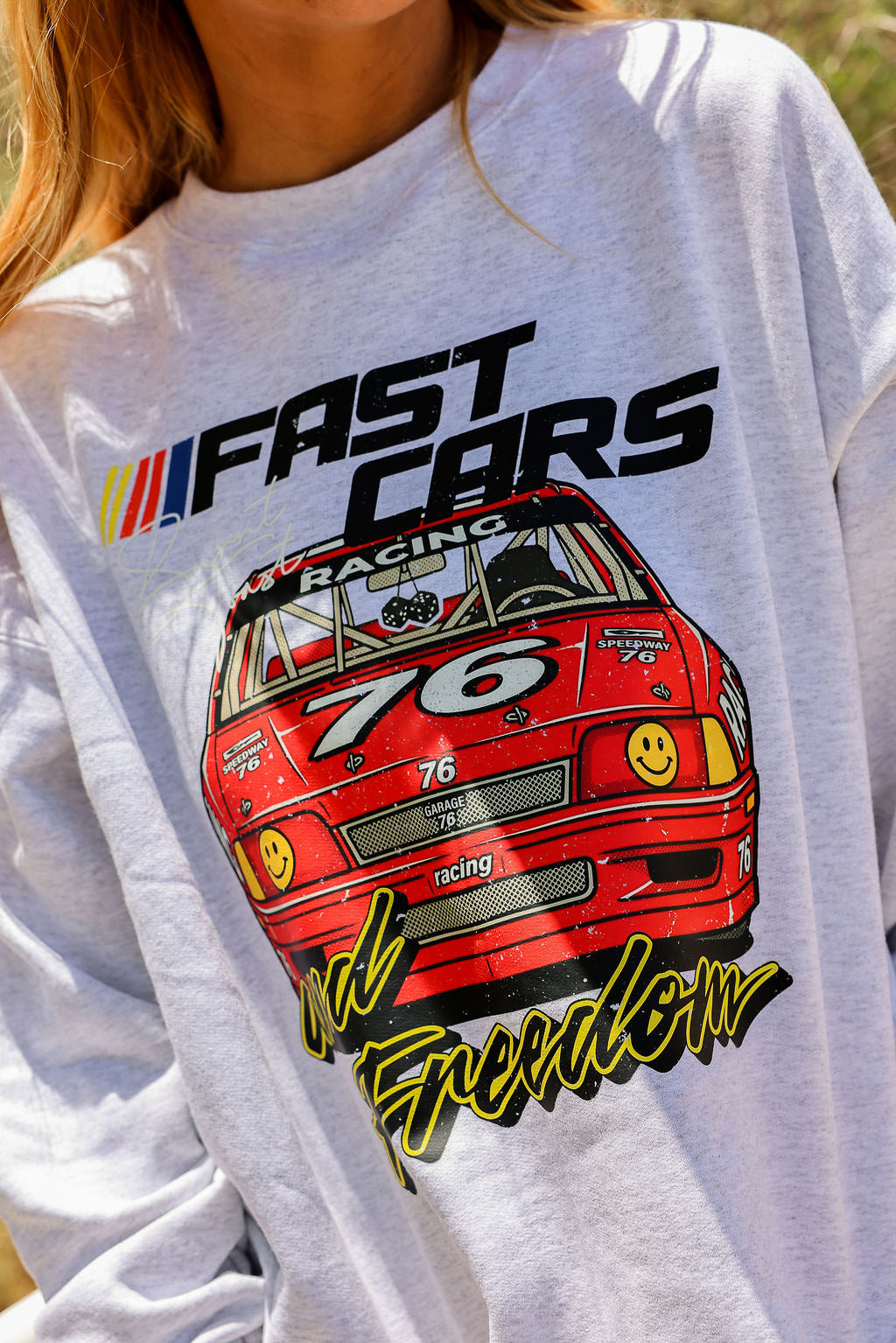 Grey crewneck with red car graphic and text on a person wearing it, close up frontal view