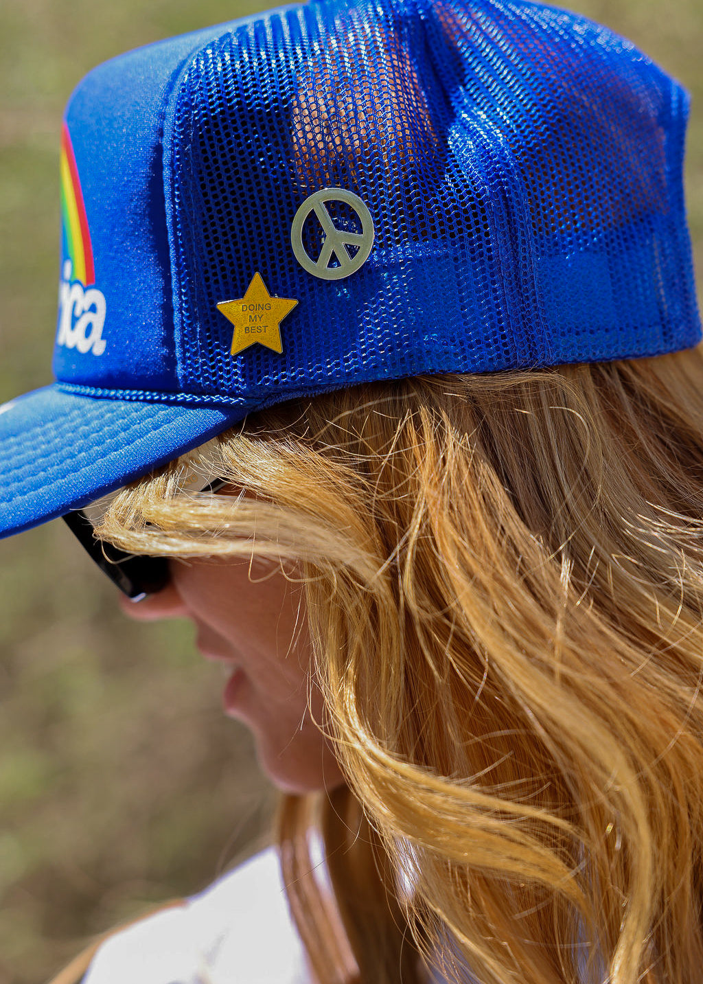Person wearing a blue mesh trucker hat with a star and peace symbol pins, side view