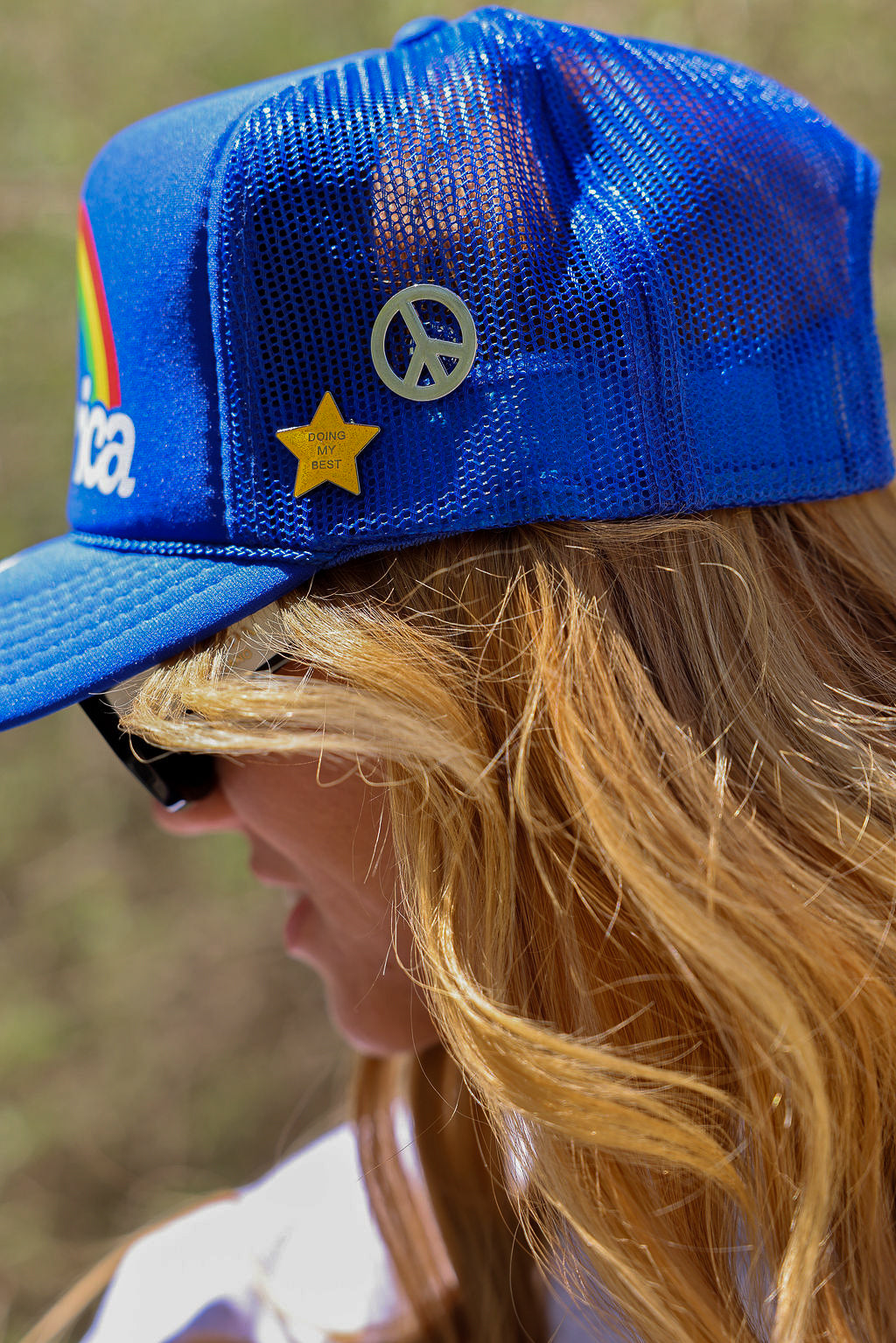 Person wearing a blue mesh trucker hat with a star and peace symbol pins, side view