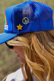 Person wearing a blue mesh trucker hat with a star and peace symbol pins, side view