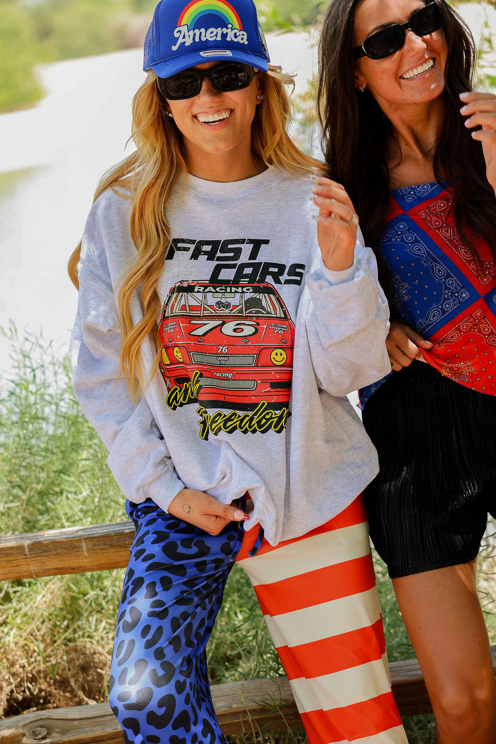 Two women outdoors, one wearing a 'Fast Cars' sweatshirt and colorful pants, the other in sunglasses and a colorful top