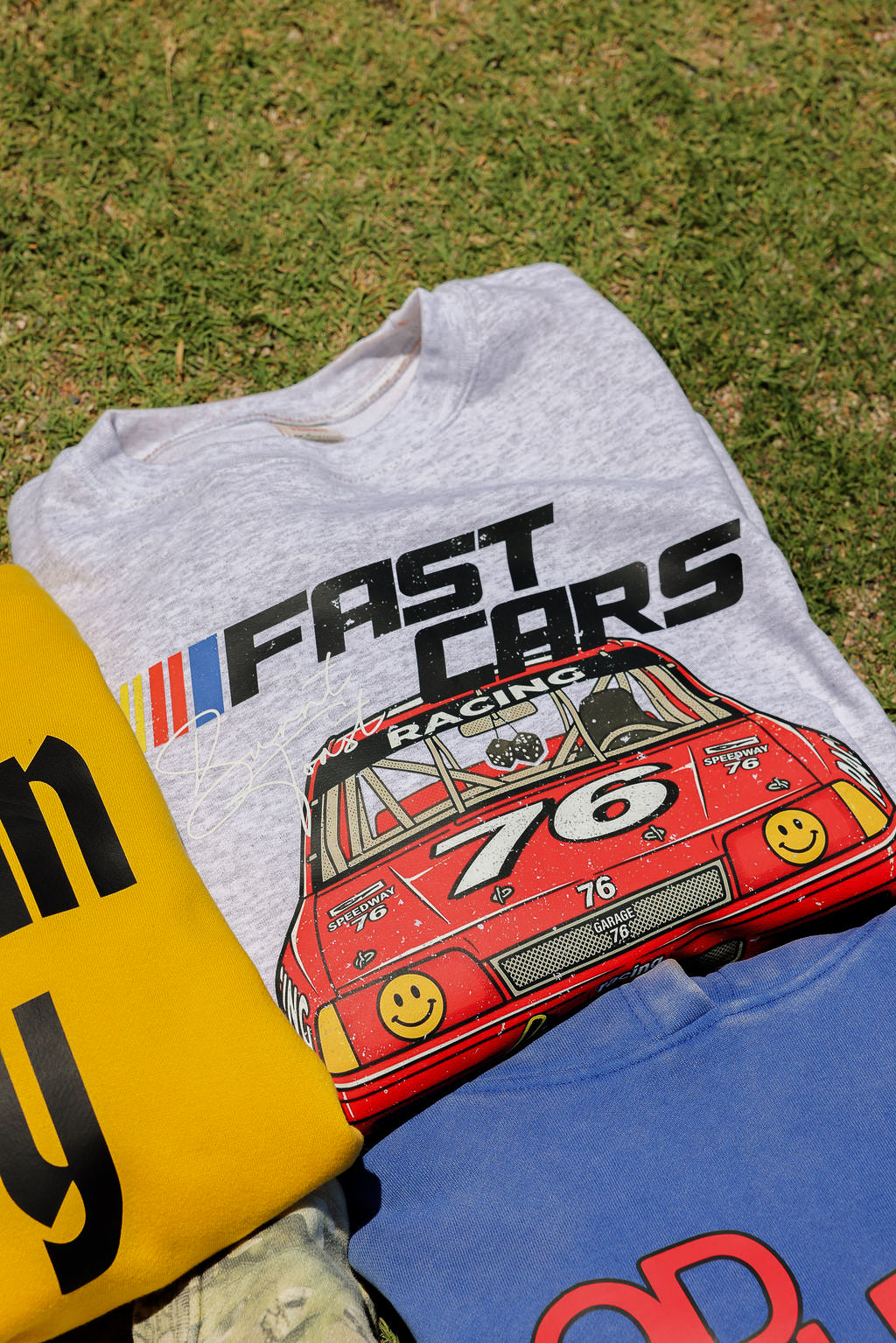 Gray sweatshirt with red race car graphic and 'Fast Cars Racing' text on grass.