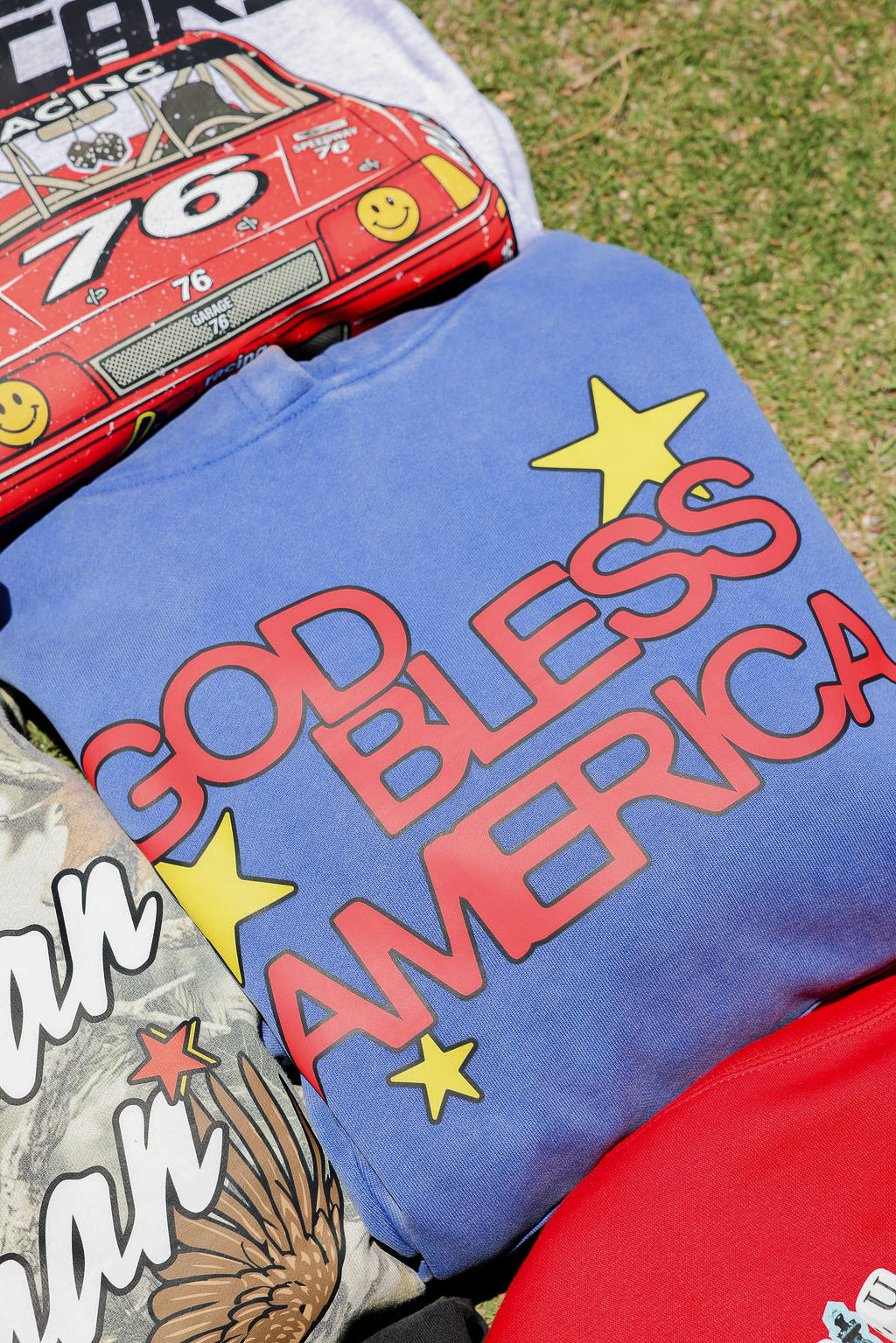Blue folded t-shirt with 'GOD BLESS AMERICA' text and stars, placed on grass.