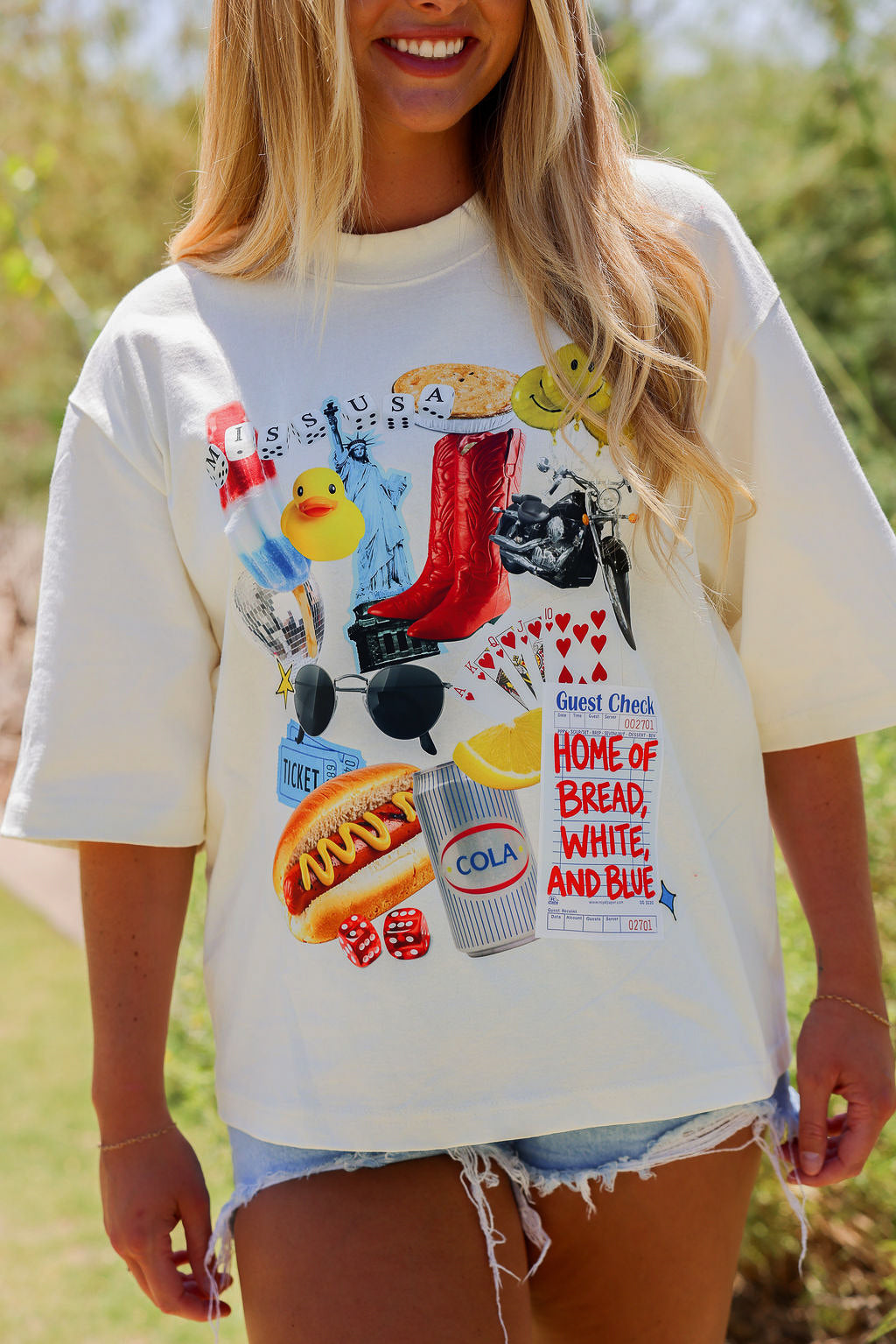 Person wearing a ivory t-shirt with colorful graphic design outdoors, frontal view