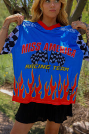Person holding a blue 'Miss America Racing Team' jersey with flames and checkered flags, close up frontal view