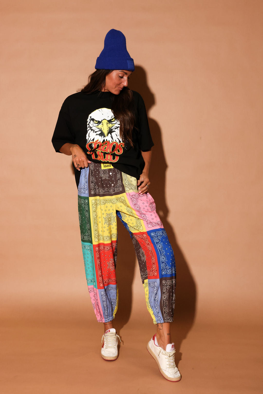 Model wearing a black t-shirt with an eagle graphic and colorful pants against a beige background, frontal view
