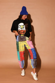 Model wearing a black t-shirt with an eagle graphic and colorful pants against a beige background, frontal view