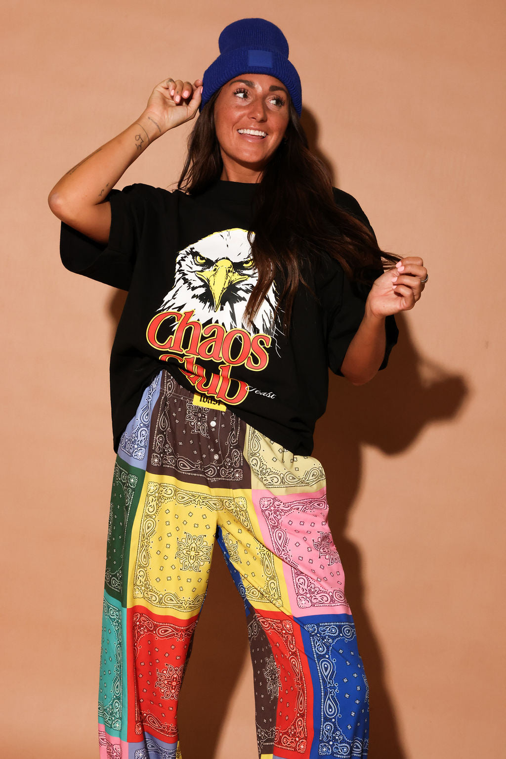 Person wearing a black t-shirt with an eagle graphic and colorful bandana-patterned pants against a beige background, close up frontal view