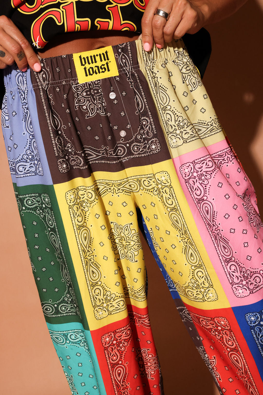 Colorful bandana-patterned pants displayed against a brown background, focus on waistband