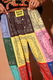 Colorful bandana-patterned pants displayed against a brown background, focus on waistband