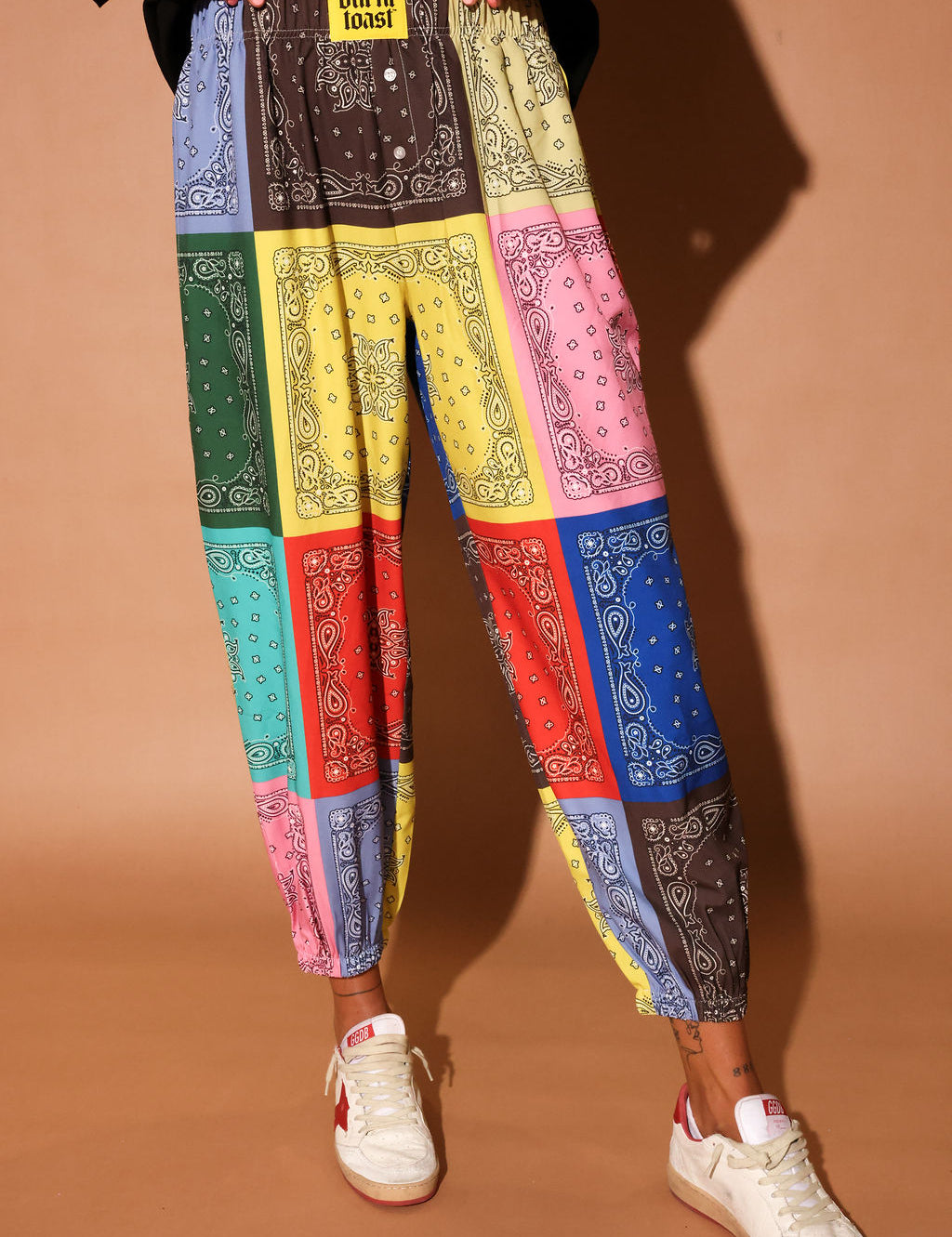 Colorful bandana print pants worn by a person on a brown background, close up view