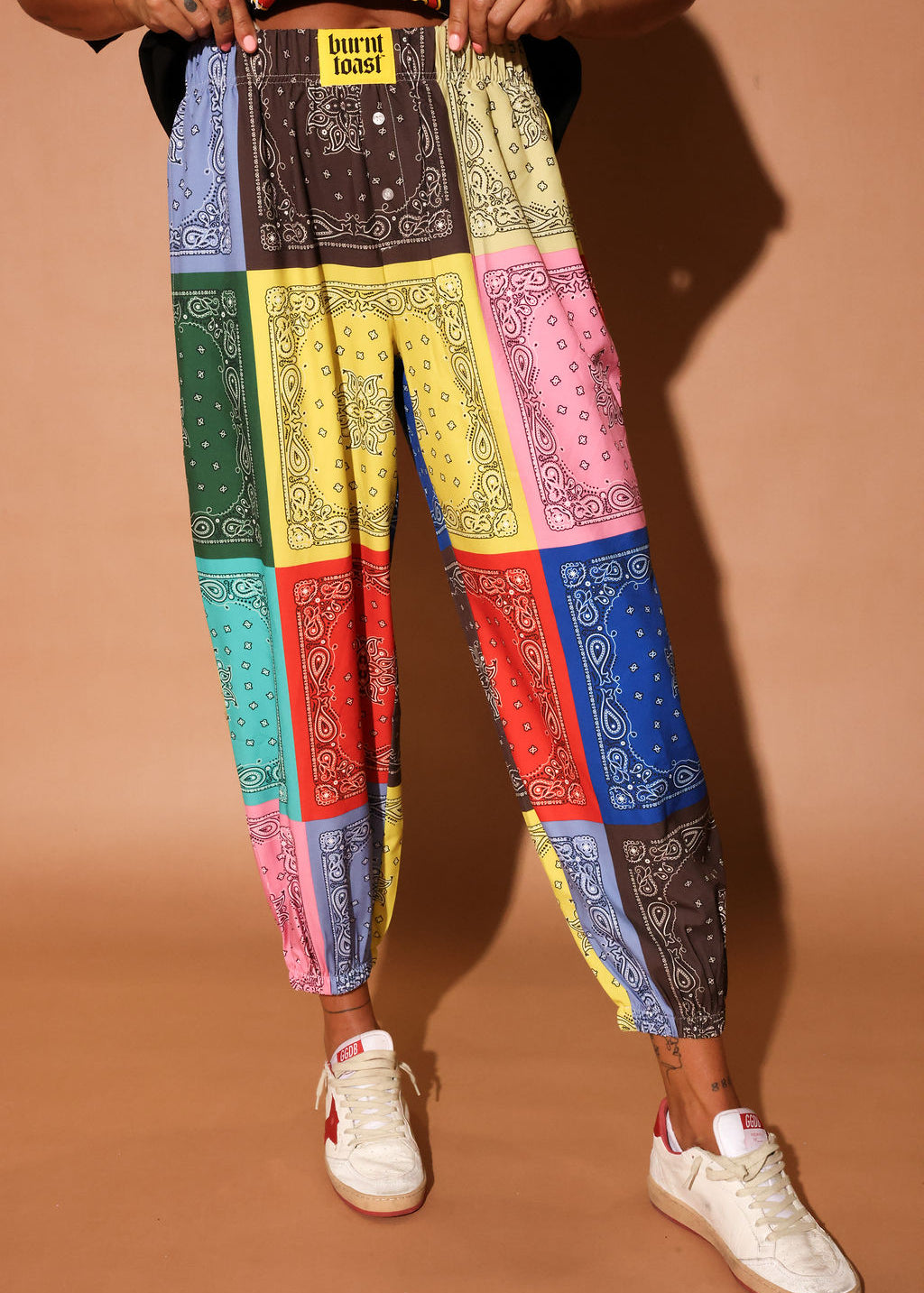 Colorful bandana print pants worn by a person on a brown background, close up view