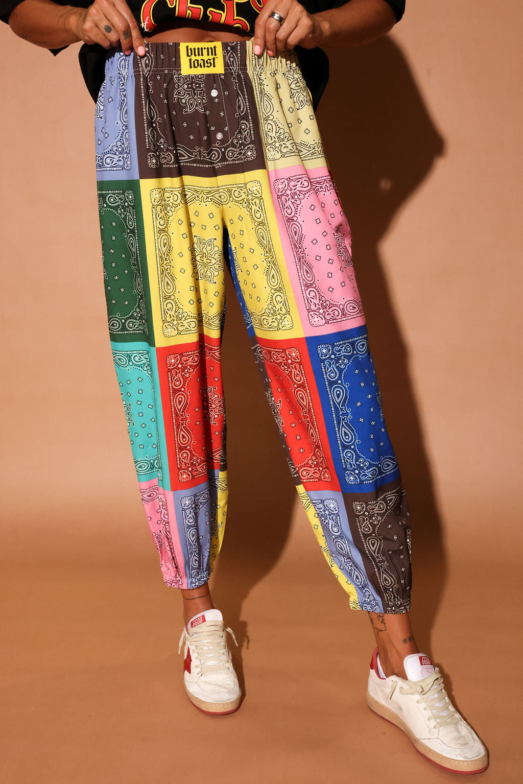 Colorful bandana print pants worn by a person on a brown background, close up view