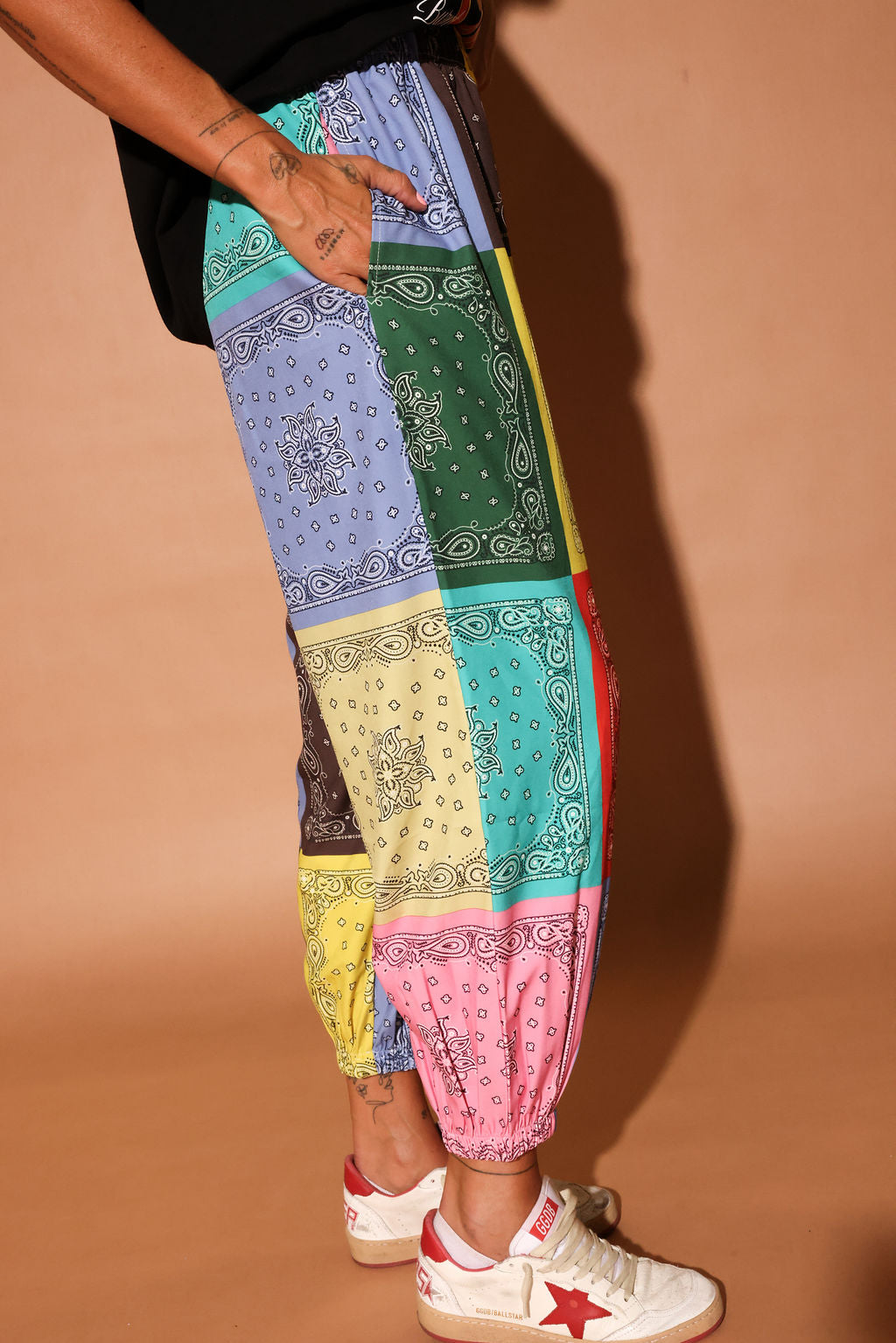 Colorful bandana pants with a patterned bandana design worn by a person on a beige background, side view