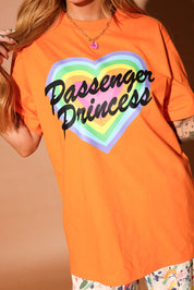 Model wearing an orange t-shirt with 'Passenger Princess' design on a brown background, close up view
