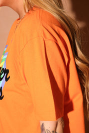 Person wearing an orange shirt with a rainbow design and text, side view