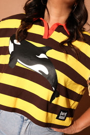 Model wearing a yellow and brown striped polo with an orca whale design and 'burnt toast' logo, close up frontal view