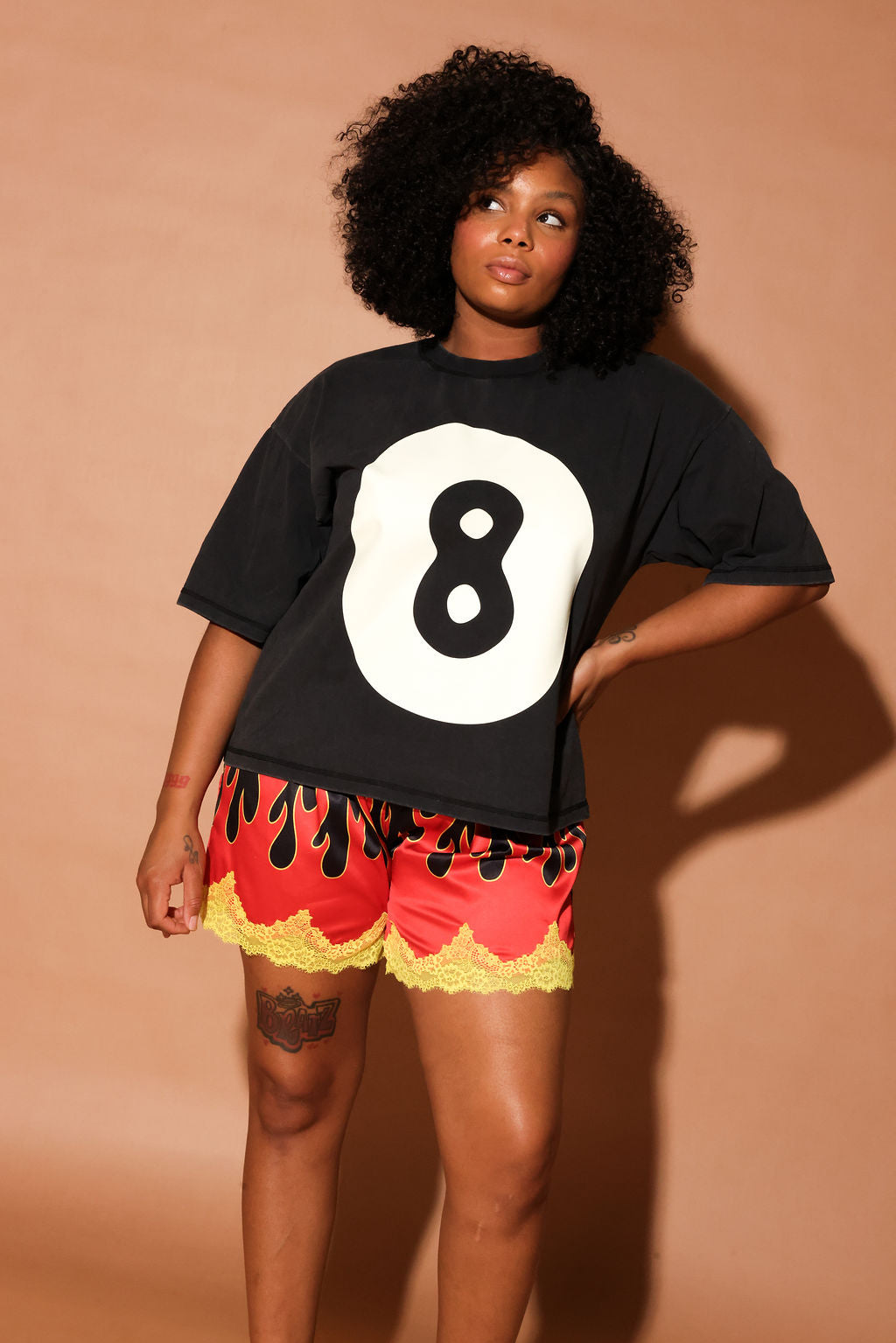 Woman wearing a black t-shirt with the number 8 and red shorts with yellow trim against a beige background, frontal view