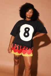 Woman wearing a black t-shirt with the number 8 and red shorts with yellow trim against a beige background, frontal view