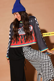 Person wearing a colorful mesh jersey with graphic design, black pants, and a blue beanie against a beige background, leaning on a ladder