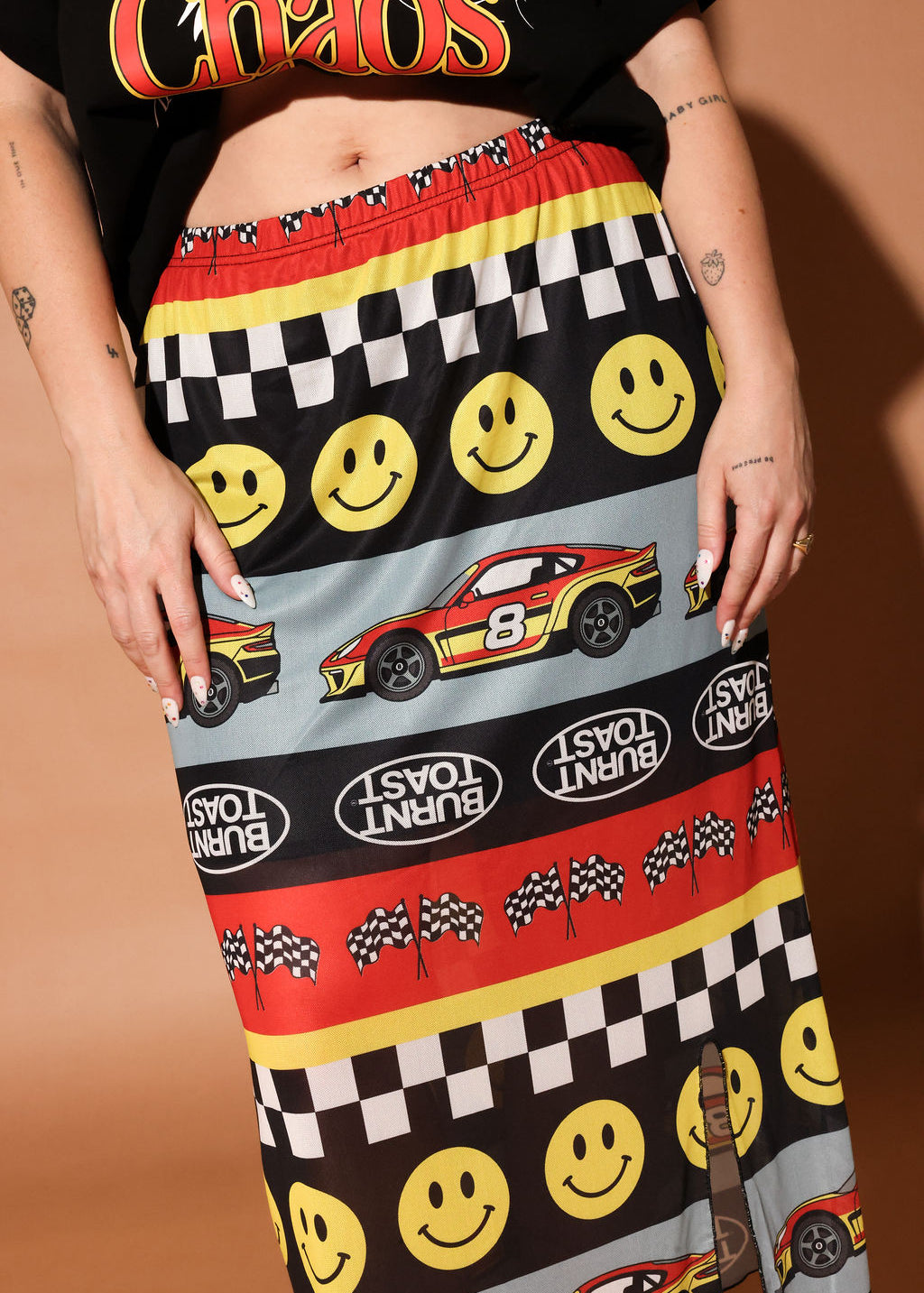 Person wearing a colorful skirt with smiley faces, cars, and checkered patterns on a brown background, frontal view