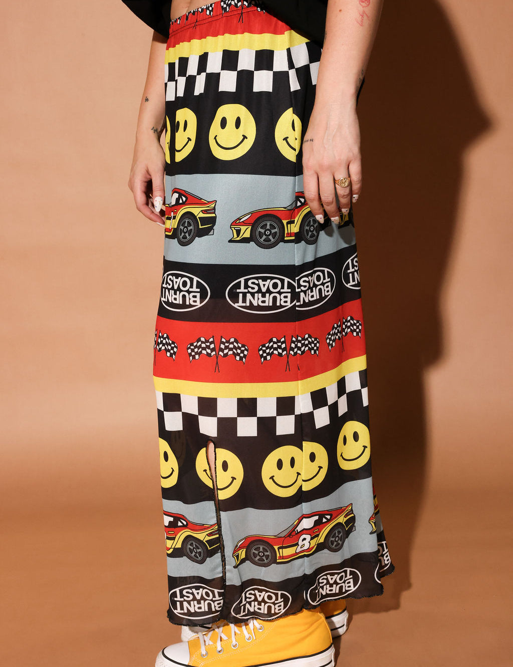 Person wearing a colorful skirt with smiley faces, cars, and checkered patterns on a brown background, side view