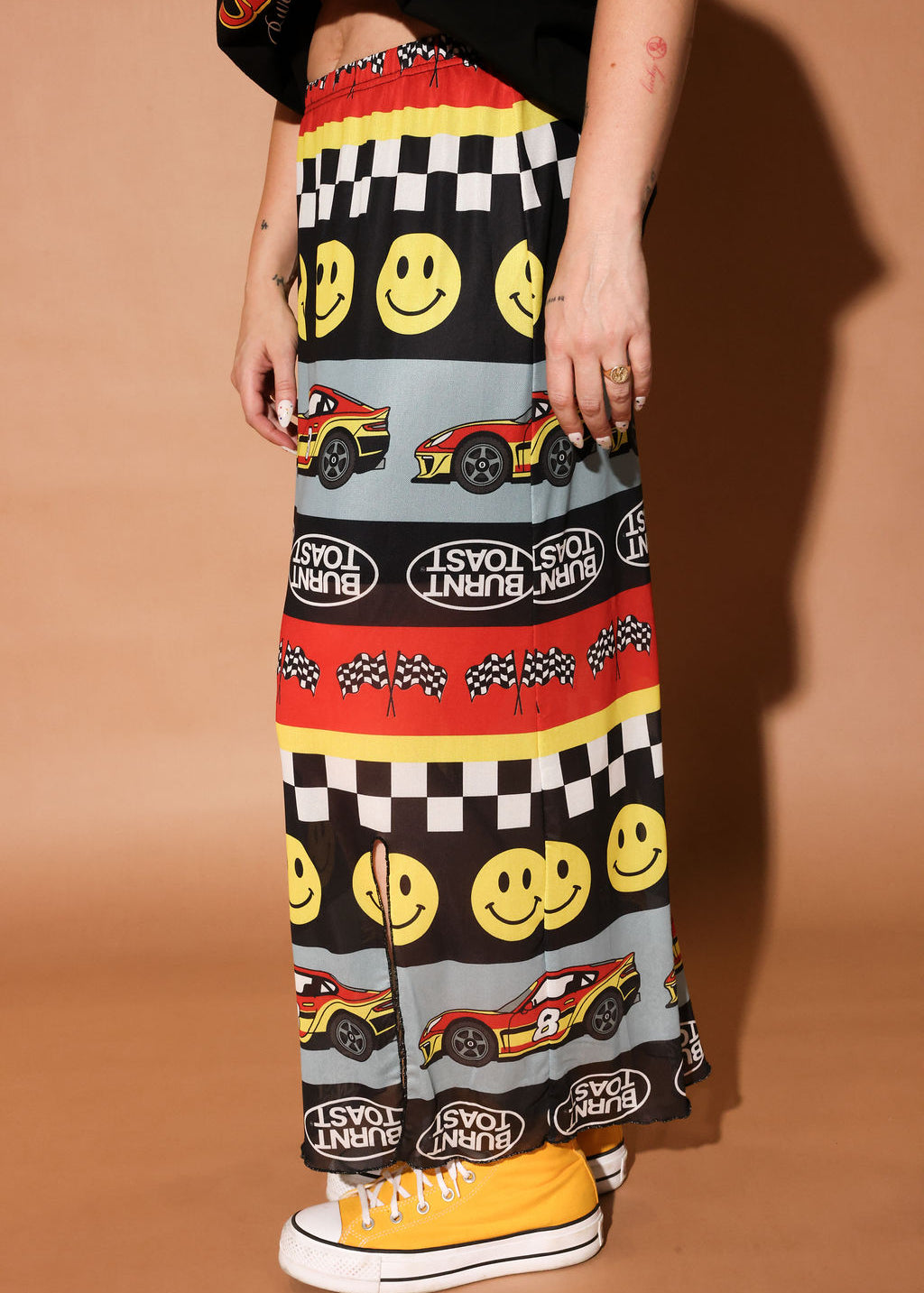 Person wearing a colorful skirt with smiley faces, cars, and checkered patterns on a brown background, side view
