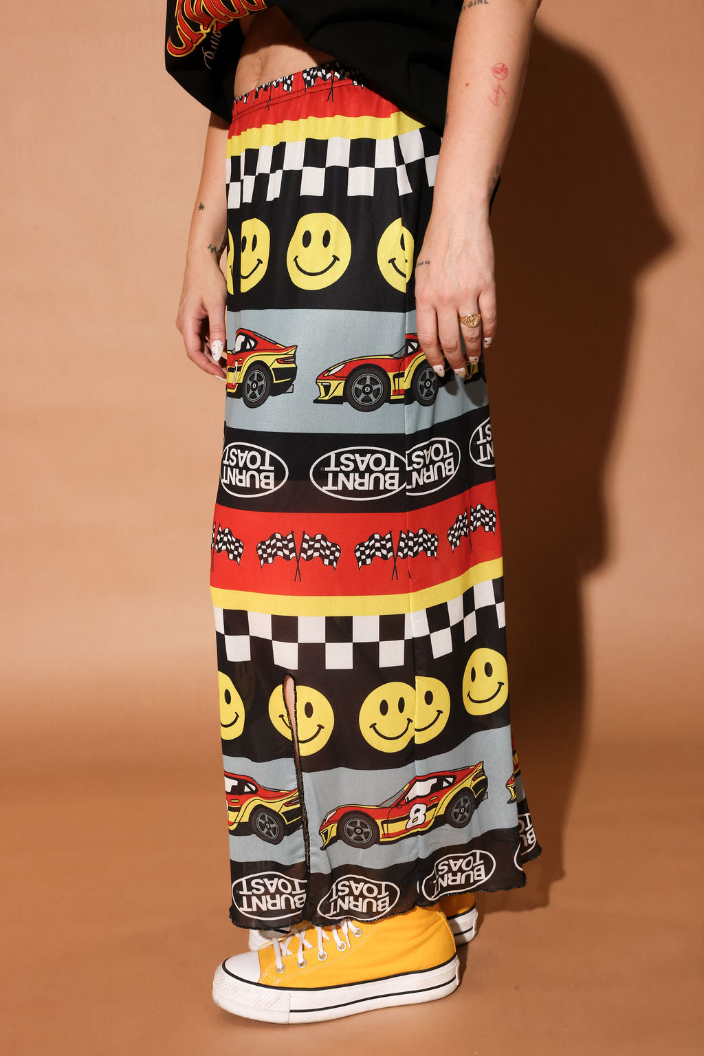 Person wearing a colorful skirt with smiley faces, cars, and checkered patterns on a brown background, side view