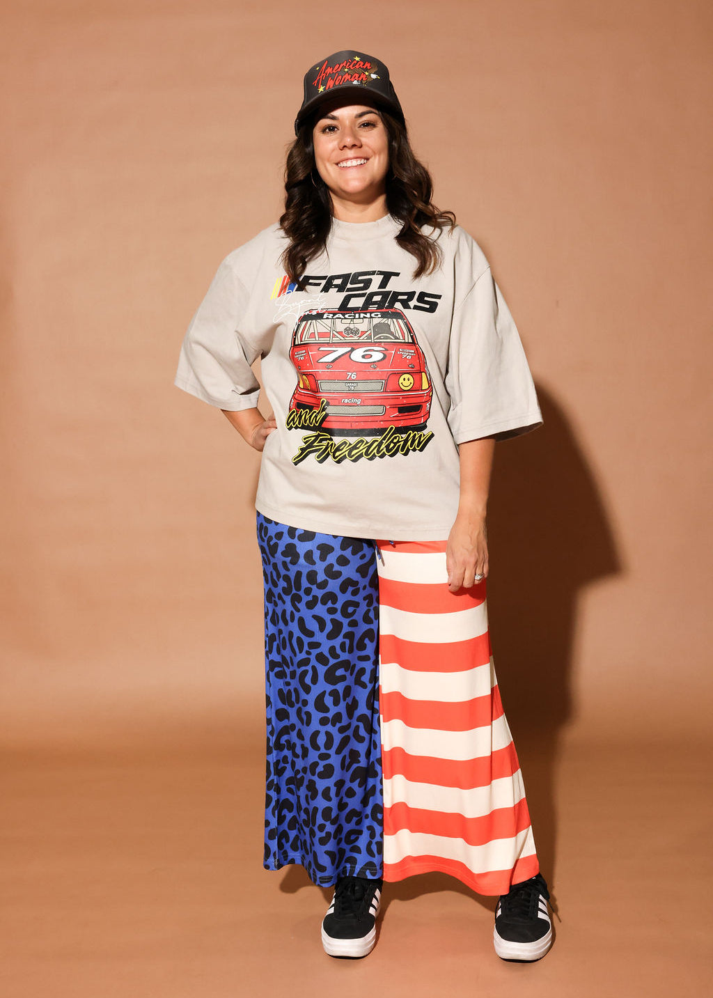 Person wearing a graphic t-shirt, cap, and colorful pants on a brown background, frontal view