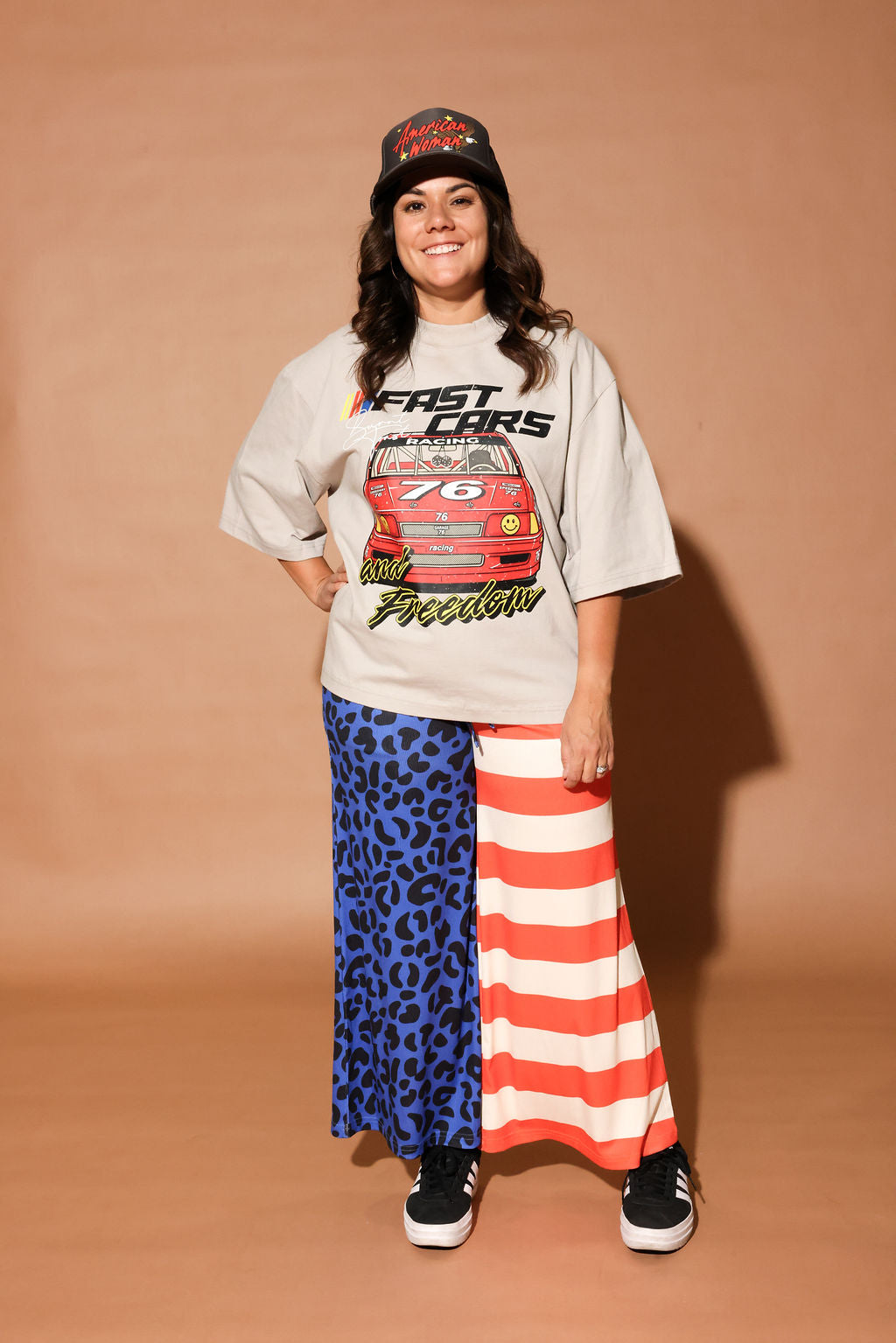 Person wearing a graphic t-shirt, cap, and colorful pants on a brown background, frontal view