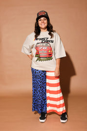 Person wearing a graphic t-shirt, cap, and colorful pants on a brown background, frontal view