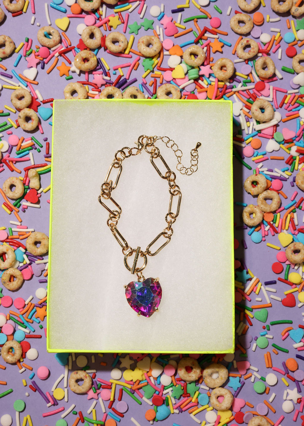 Bracelet with a heart-shaped multicolored pendant on a colorful background with sprinkles and cereal