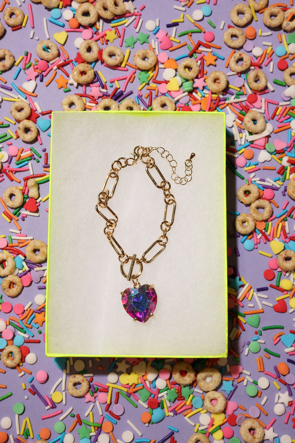 Bracelet with a heart-shaped multicolored pendant on a colorful background with sprinkles and cereal