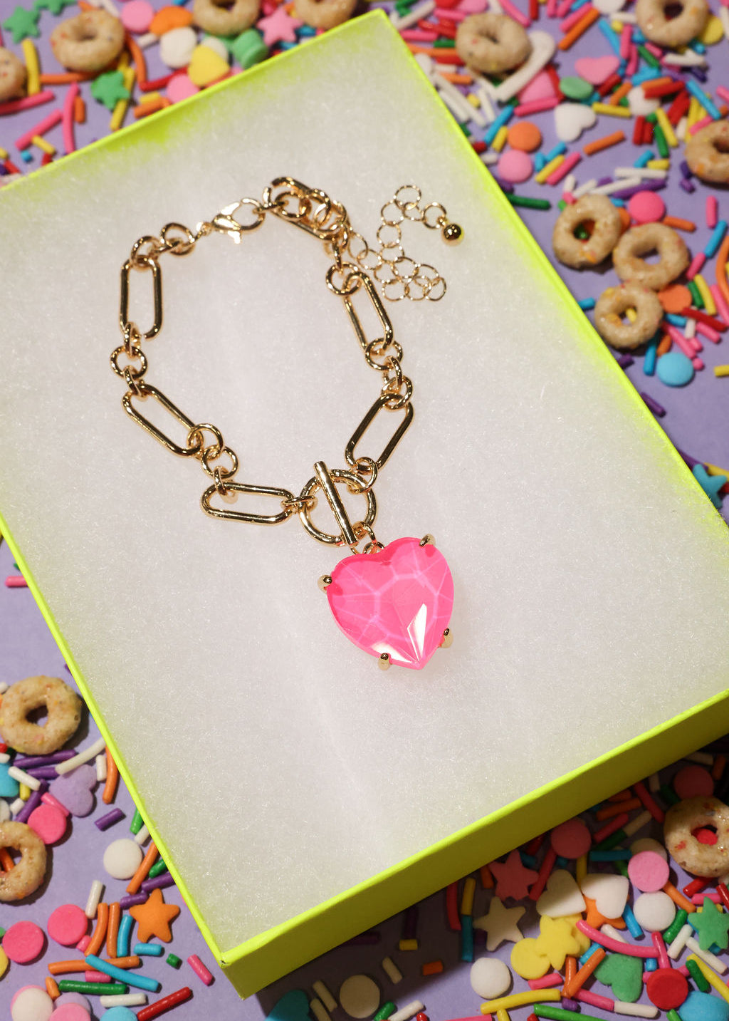 Gold bracelet with a pink heart charm on a colorful background